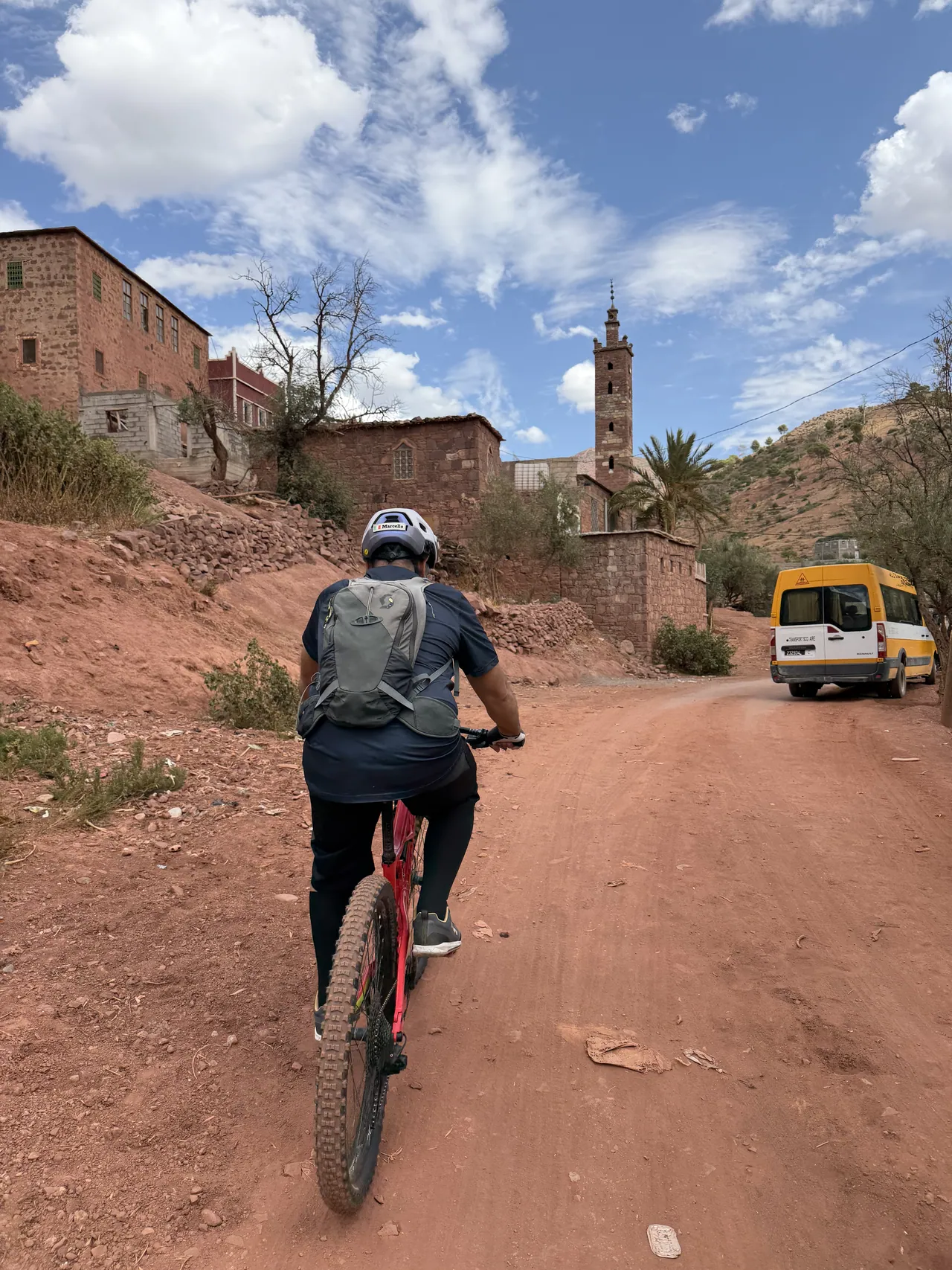 A rider heads through a village on a red dirt road – cross-country mountain bike tour in Morocco